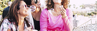 Drei Frauen mit Seifenblasen sitzen auf Treppe und lachen