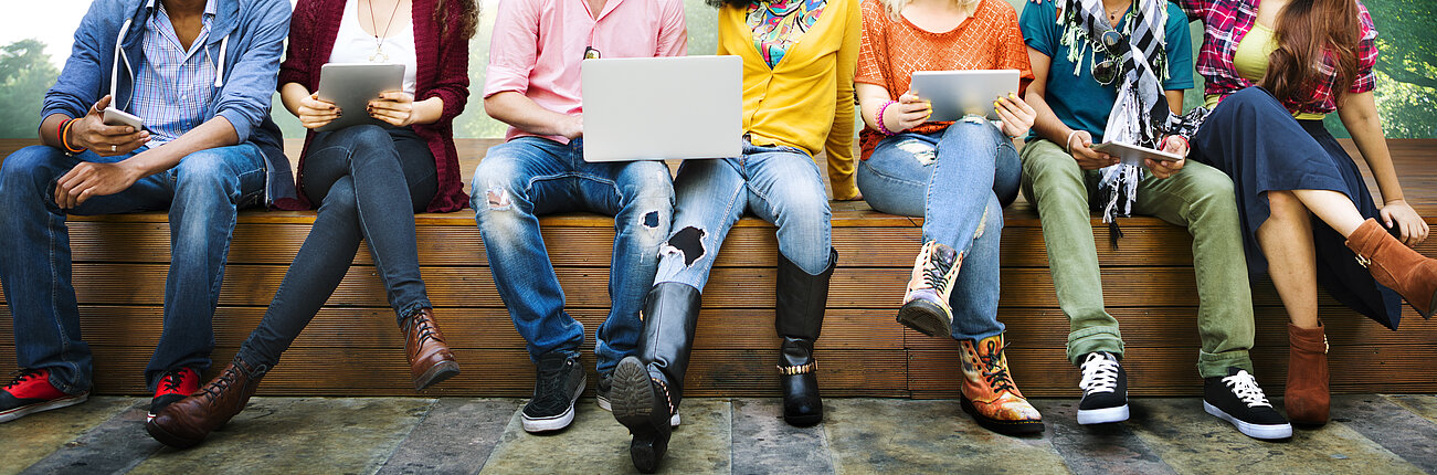 Jugendliche sitzen am Smartphone und Laptop.