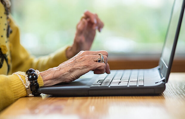 Nahaufnahme von Händen einer alten Frau, die am Laptop auf der Tastatur tippt